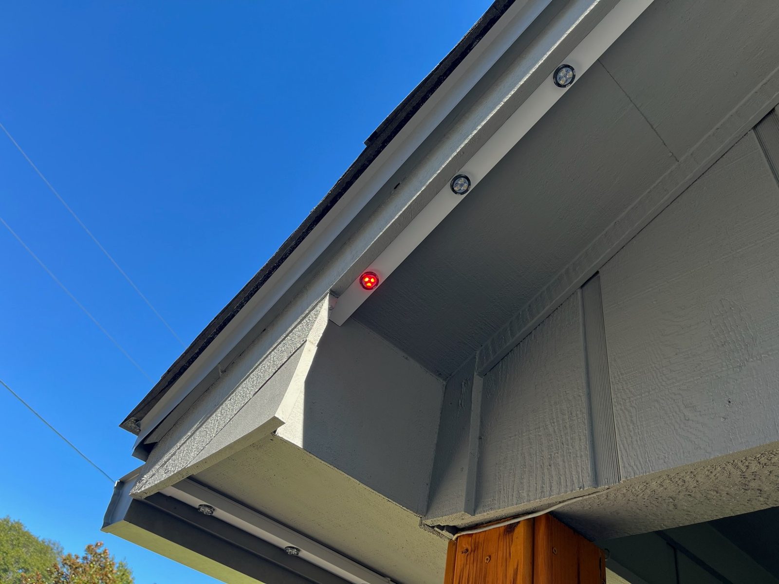 A finished porch corner by day: white track under the eave, one puck lit red, no screws or wires visible.
