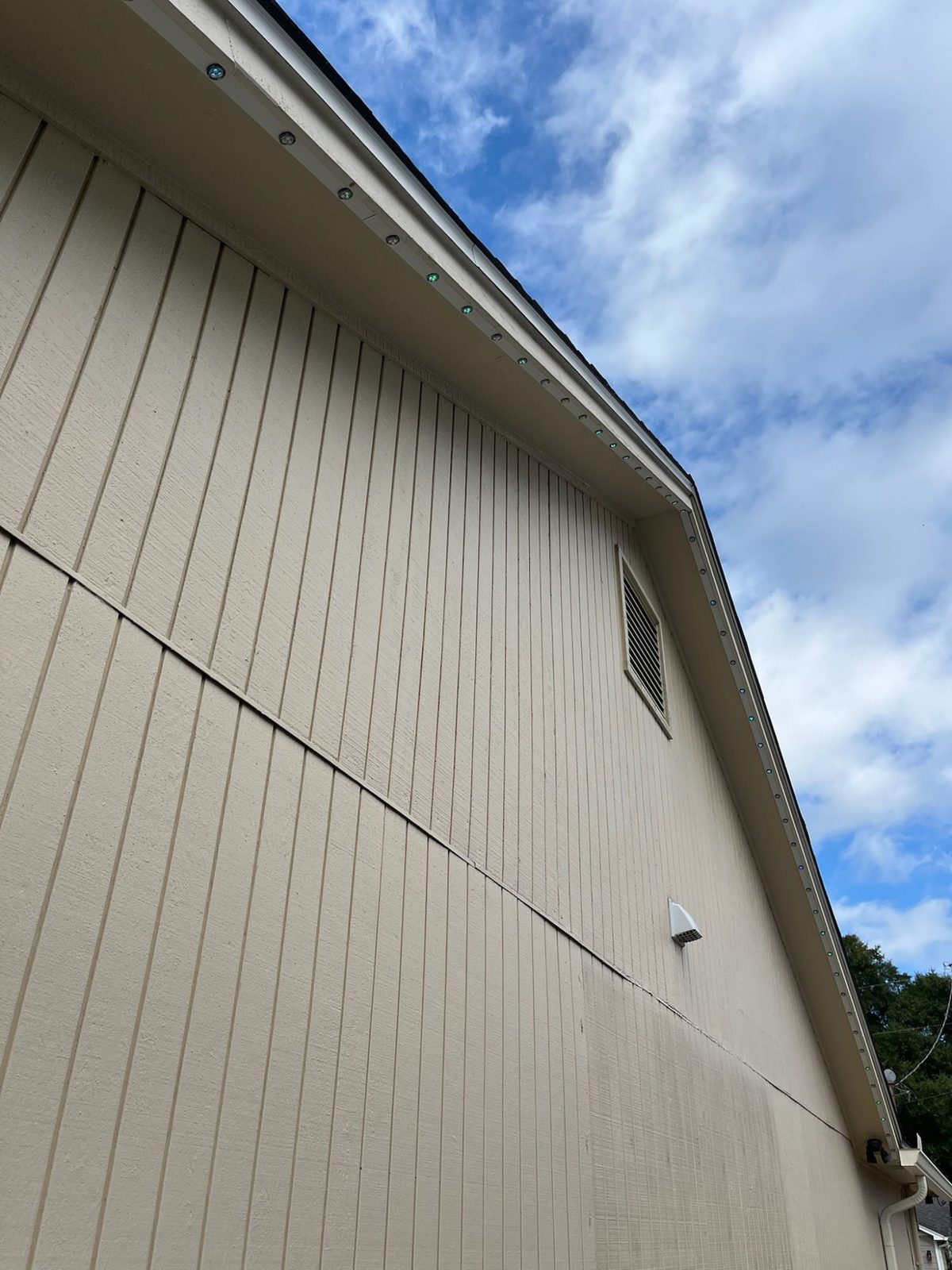 A gable by day: puck lights in white track follow the rake up to the peak and back down, with no wires showing.