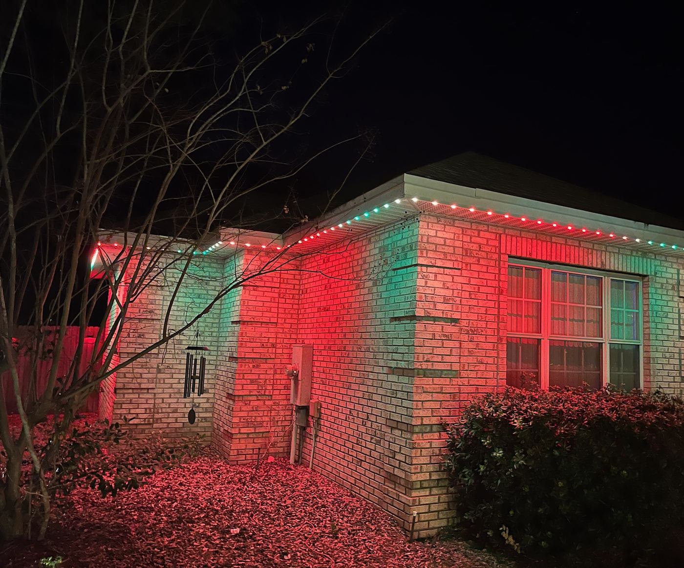 A finished install at night: puck lights along a brick home&rsquo;s eave in red, white and green, with no visible wires.