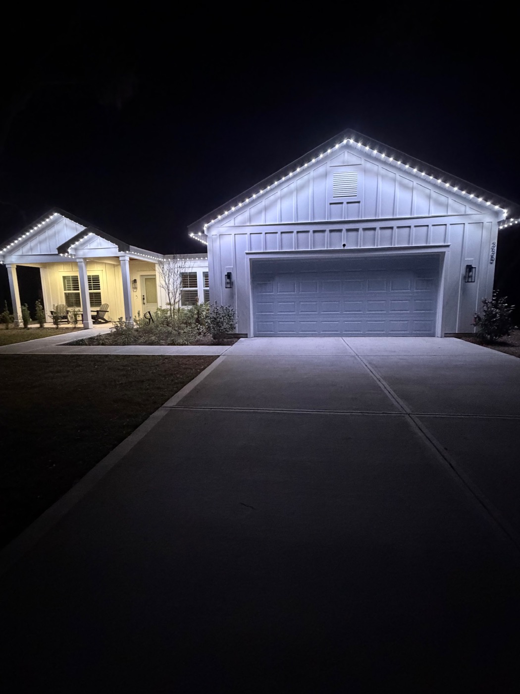 A white farmhouse-style home outlined in bright white permanent lights at night.