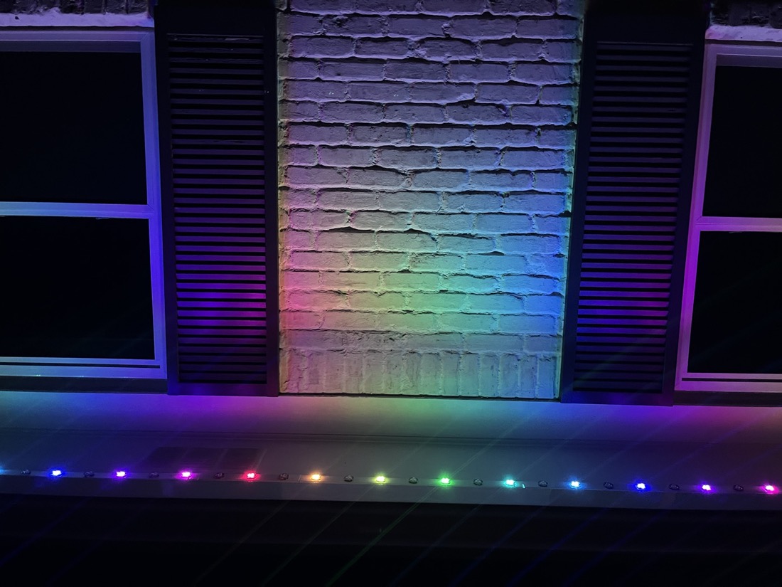 Chameleon puck lights in rainbow colors along a roof eave.